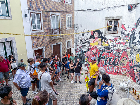 a group of tourists listen to the explanations of a free tour guide in front of a graffiti with drawings referring to the history of fado in the streets of the historical center of lisbon