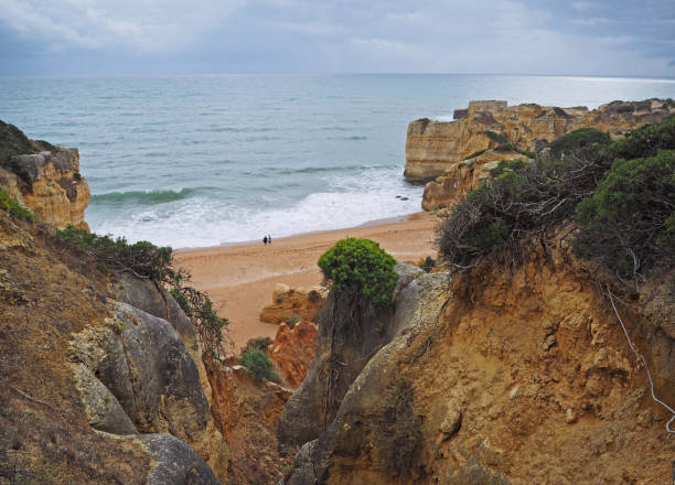 istock beautiful sandstone cliffs with view on two people standing on sand beach with sea waves and rock formation and blue sky background in Algarve 1415240115
