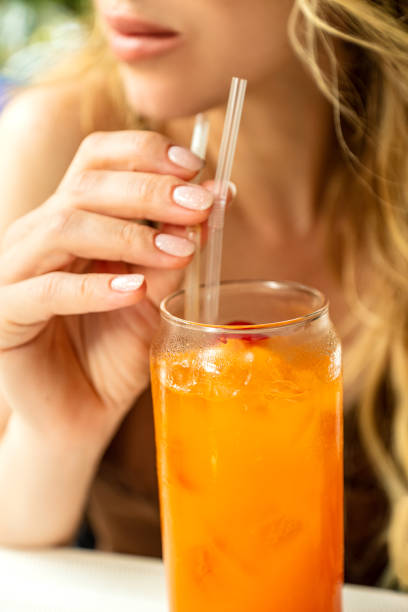istock Young woman drinks fruit cocktail or freshly squeezed juice or refreshing drink and holds sipping straw with her fingers 1415241858