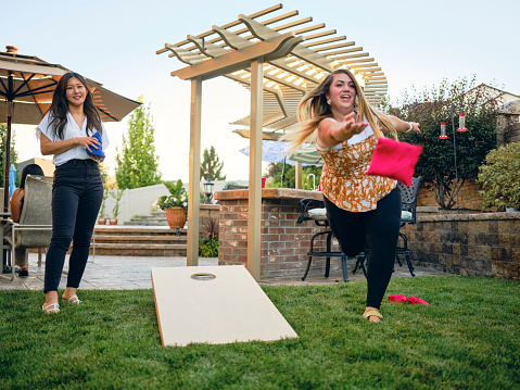 A group of friends playing a Cornhole bean bag toss game in a backyard of a home.