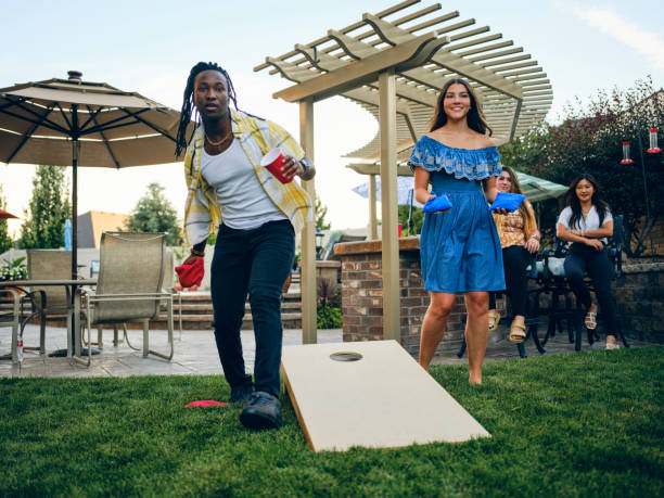 Backyard Party Playing Cornhole Bean Bag Toss Game A group of friends playing a Cornhole bean bag toss game in a backyard of a home. backyard party stock pictures, royalty-free photos & images