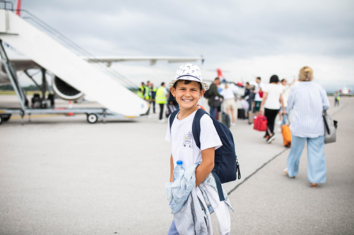 A cute boy is happily smiling at the camera about to board a plane