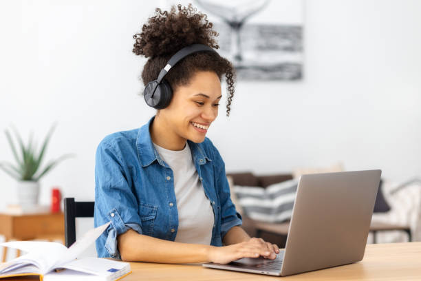 istock Smiling woman student online learning at home. Beautiful African American female student using laptop computer and video call for distance education, studying 1415248083