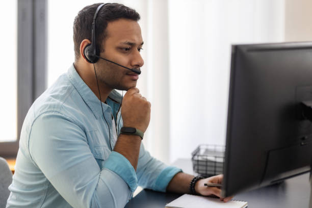 Concentrated man call center worker in headphones is working at modern office. Portrait of Asian male support employee stock photo