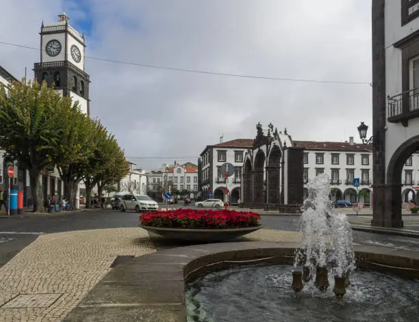 Portugal, Ponta Delgada Sao Miguel, Azores, December 21, 2018: Main square of Ponta Delgada and view on Portas da Cidade -Gates to the City, church of St. Sebastian red blooming flowers and fontain.