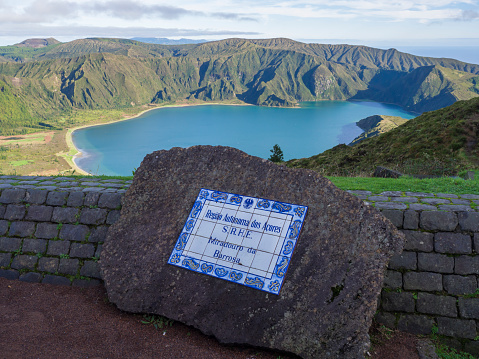 View on beautiful blue crater lake Lagoa do Fogo from viewpoint miradouro da barrosa. and sign on ceramic deskon stone. Lake of Fire is the highest lake of Sao Miguel island, surrounded by Natural Reserve green.
