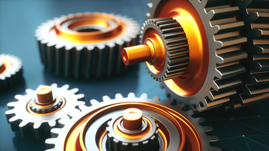 Extreme close up on a shiny gear mechanism with several orange colored gears on a dark surface.