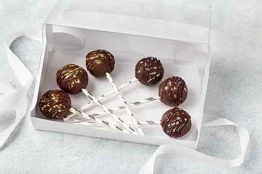 Delicious dessert with chocolate and milk cream on a stick. cake pops in a white box with a ribbon on a white background