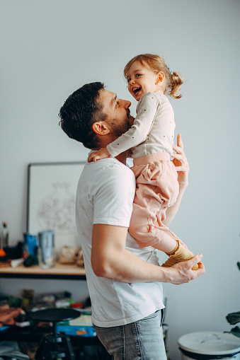 Handsome man is holding his daughter's legs while she is trying to stand in the air. She is laughing while trying to hold balance.