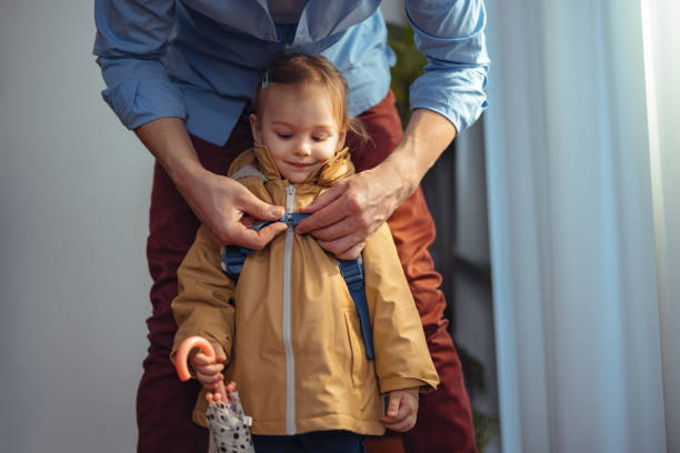 Anonymous Dad Getting His Daughter Ready to Go Outside Close up shot of an unrecognizable father dressed up for work, standing behind his daughter preparing her to go outside with him. He is adjusting the straps of her backpack while she is smiling and looking down. girls getting ready to go out stock pictures, royalty-free photos & images