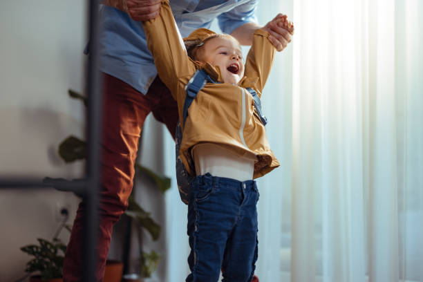 Anonymous Dad Getting His Daughter Ready to Go Outside Unrecognizable father ready for work standing behind his daughter playing with her before they go outside. She is all dressed up with her yellow rain coat. He is holding her by her both hands and pulling up while she looks excited. girls getting ready to go out stock pictures, royalty-free photos & images