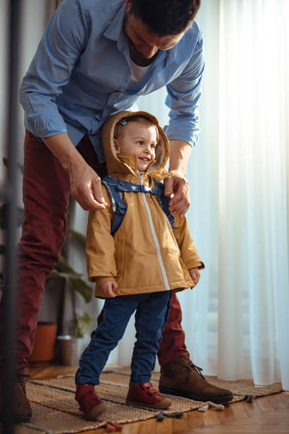 Portrait of an Unrecognizable Man Getting His Daughter Ready to Go Outside Portrait of a cute little girl getting dressed to go outside. Her unrecognizable father is standing behind her zipping her jacket. She is looking forward and smiling. girls getting ready to go out stock pictures, royalty-free photos & images