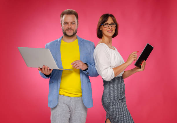 Two professional with a tablet and a laptop on a pink background. A team of two business people of business partners is used by a tablet and laptop. stock photo