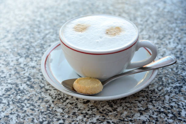 cappuccino avec du lait moussé dans une tasse blanche et un biscuit sur une cuillère, boisson chaude servie sur une table en pierre de granit, espace de copie, focus sélectionné, - foamed milk photos et images de collection