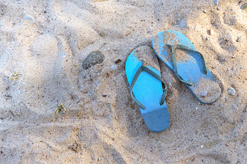 Summer vacations on the beach, blue flip-flops in the sand in a tourist resort on the Baltic Sea in Germany, copy space, selected focus, high angle view from above