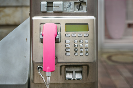 Public pay phone made of scratched metal with a pink handset, insert for coins and credit card, in Germany, copy space, selected focus