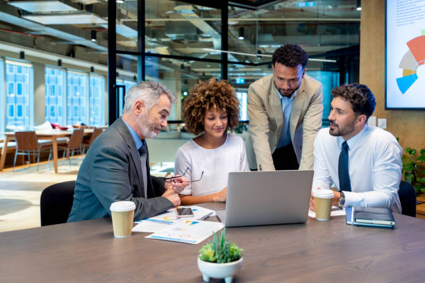 Four business people working on a laptop computer in an office.