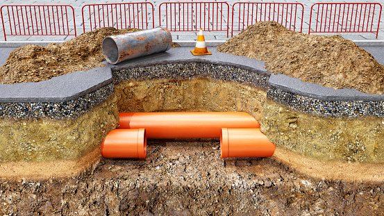 Concept of road works and underground pipes renovation, new orange pvc pipes are installed instead of old rusty section, slice of ground and a pit digged in the asphalt, mounds of soil are upside with road cone and fences, 3d illustration