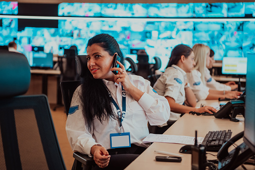 Female security guard operator talking on the phone while working at the workstation with multiple displays Security guards working on multiple monitors. High quality photo