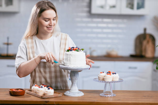 キッチンテーブルにケーキを持つパティシエ菓子の若い白人女性。 - cake women confectioner photography ストックフォトと画像