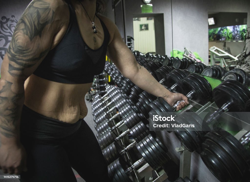 Body positive woman chooses a dumbbell for exercise Body positive woman Body positive woman chooses a dumbbell for exercise in gym Athlete Stock Photo