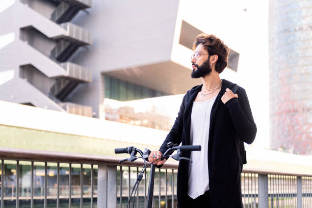 young caucasian man with beard wearing trendy clothes and walking with his folding bike through the city, concept of urban lifestyle and sustainable mobility, copy space for text
