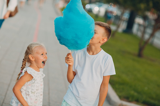 Happy children boy and girl eating blue cotton candy outdoors.