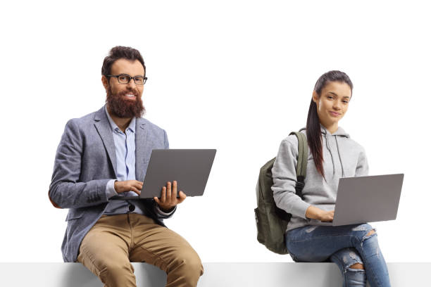 istock Female student and a bearded man sitting on a blank board with laptop computers 1415280839