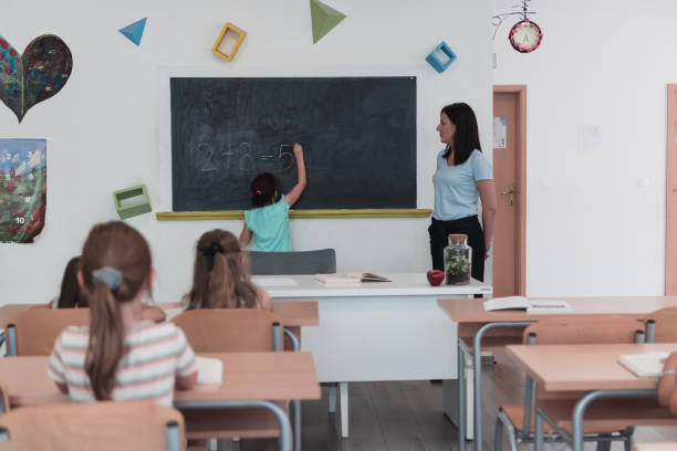 szkoła podstawowa. nauczycielka pomaga uczniowi dziecka podczas pisania odpowiedzi na tablicy. - professor adult student chalk drawing formula zdjęcia i obrazy z banku zdjęć