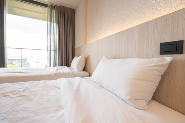 흰색 침구가있는 싱글 침대 2 개는 헤드 보드 조명을 켜고 회색 커튼을 여는 호텔의 크림 침실에 있습니다. - curtain balcony bed sheet 뉴스 사진 이미지