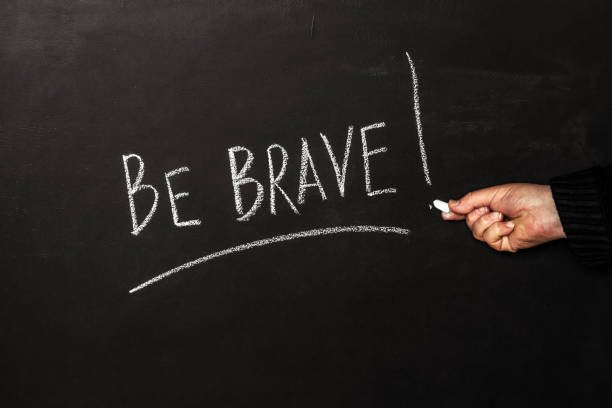 istock A man writes on a black board with white chalk the phrase Be brave! 1415287664