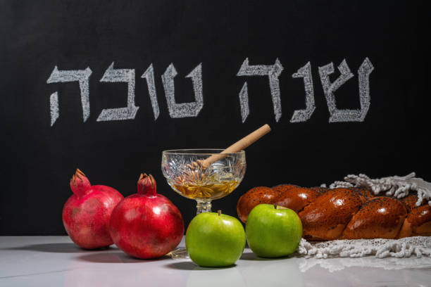 Hebrew inscription Good year (Shanah tovah) on a chalk board. Apples, pomegranates, honey and wicker challah on a wooden table. stock photo