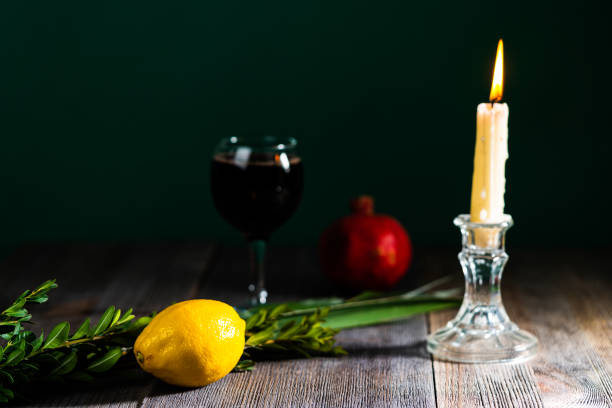 Symbols of jewish fall festival of Sukkot, lulav - etrog, palm branch, myrtle and willow next to a glass of wine and pomegranate stock photo