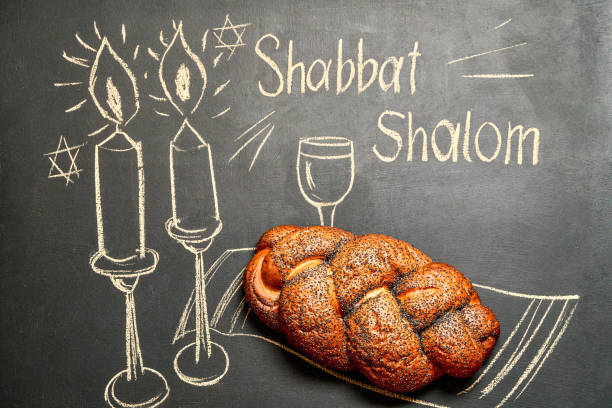 Shabbat Shalom - Jewish and Hebrew greetings. Candles and a glass of wine drawn on a chalk board next to wicker bread stock photo