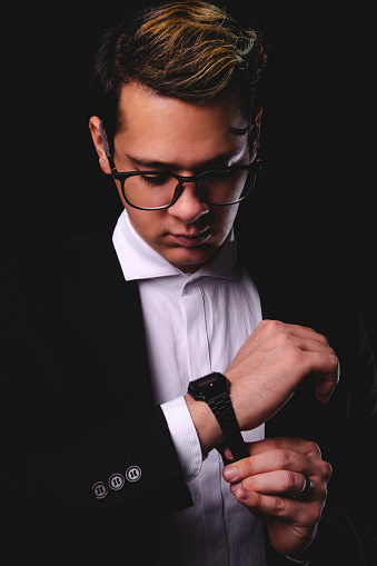 Blond boy dressed in a suit with a watch on his wrist on a black background. Business man in white shirt and black suit. Model dressed as a business executive with glasses. High quality photo