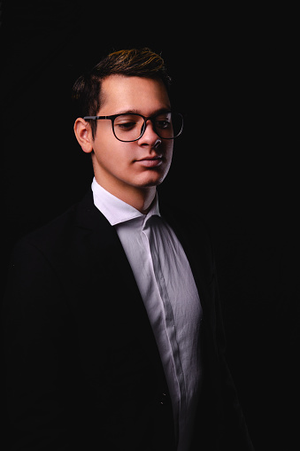 Businessman on a black background. Man dressed in a suit, white shirt and glasses. Elegantly dressed business executive. High quality photo