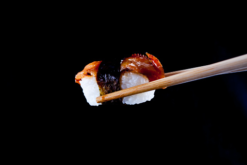 A Unagi Sushi being held by wooden chopsticks