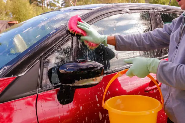 Photo of Worker washing red car with sponge on a car wash.male hand holds with green red sponge washing car. Concept car wash clean.Washing with soap.