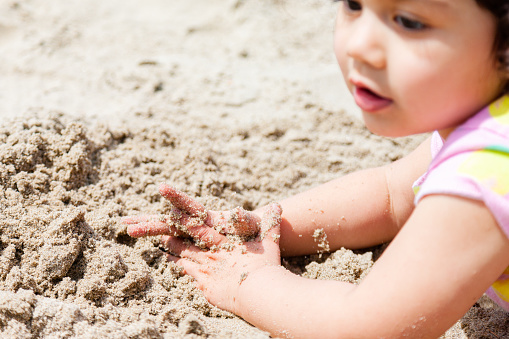 A little girl about 2 years old playing in the sand on the beach in Oregon. She is showing emotions of happiness and excitement, the weather is nice and she is having a great time
