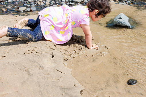 A little girl about 2 years old playing in the sand on the beach in Oregon. She is showing emotions of happiness and excitement, the weather is nice and she is having a great time