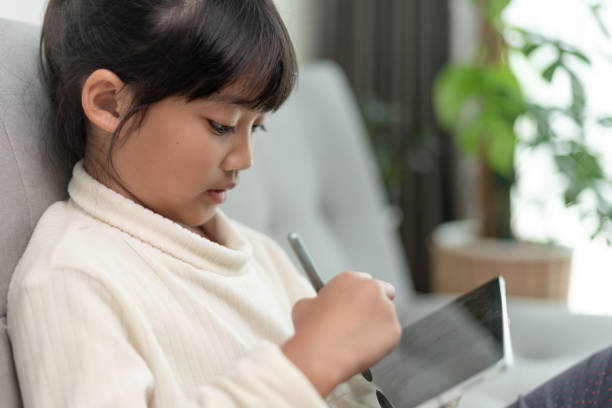 istock Little girl using tablet playing game on the internet, Kid sitting on sofa watching or talking with a friend online, Child relaxing in living room in the morning, Children with New Technology concept 1415310230
