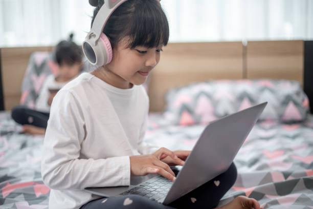istock Little Asian girl using a laptop while lying on the bed 1415310235