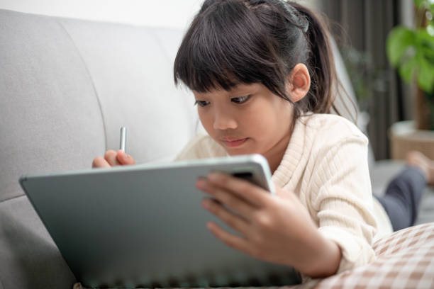 istock Little girl using tablet playing game on the internet, Kid sitting on sofa watching or talking with a friend online, Child relaxing in living room in the morning, Children with New Technology concept 1415312060