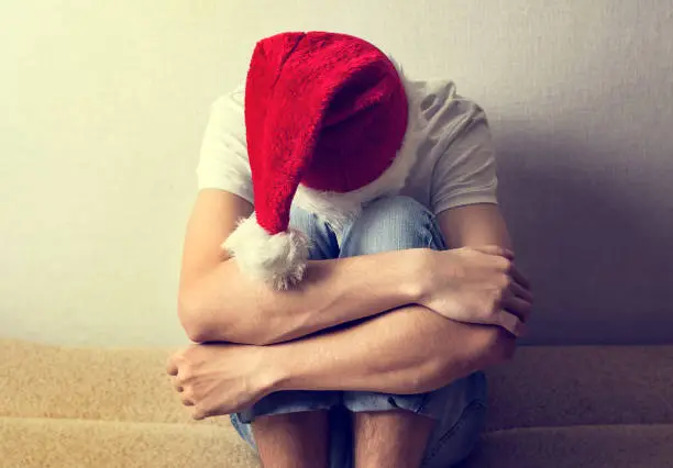 Toned Photo of Sad Young Man in Santa Hat on the Couch