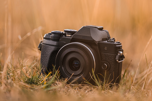 One digital photo camera without logos outdoors in dry grassland, background and foreground blurred, focus on photographic equipment, usefull for many photography themes