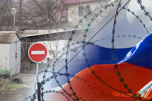 Road sign traffic is prohibited on the background of private houses and the flag of Russia behind barbed wire. Isolation of the Russian Federation from the world, sanctions against Russia