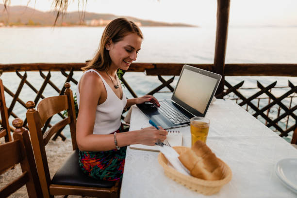 istock Smiling woman using a laptop in a restaurant during vacation 1415313272