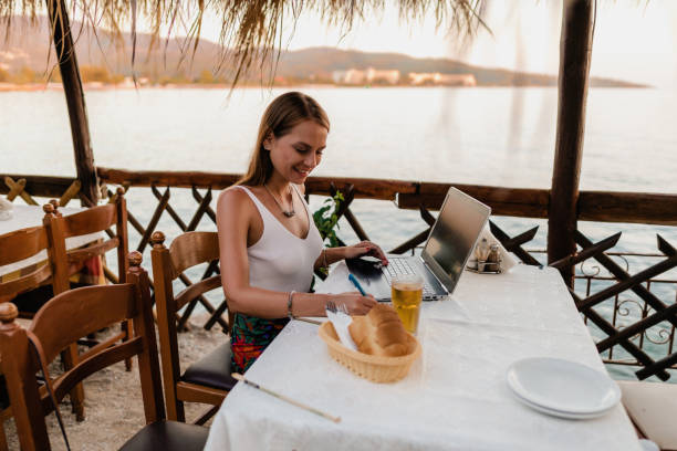 istock Smiling woman using a laptop in a restaurant during vacation 1415313290