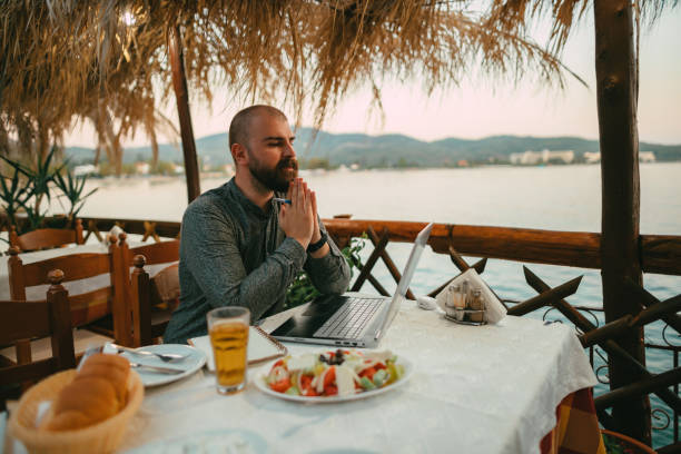 istock Bearded man using a laptop in a restaurant at the seaside 1415313303