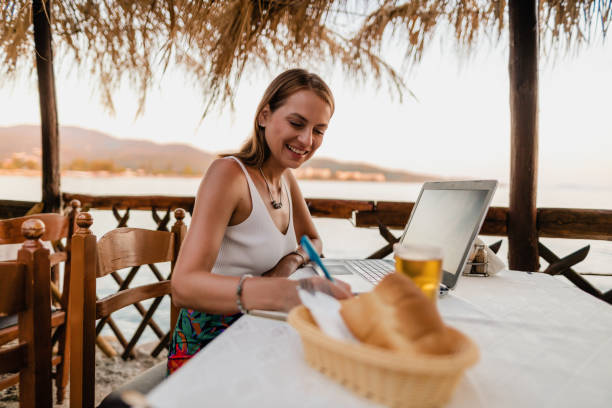 istock Smiling woman using a laptop in a restaurant during vacation 1415313312